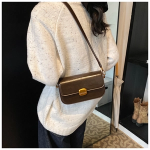Gros plan d'un sac à bandoulière en cuir verni marron avec fermoir doré sur un mannequin
