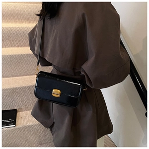 Détail du sac bandoulière en cuir verni noir avec un fermoir métallique doré de qualité