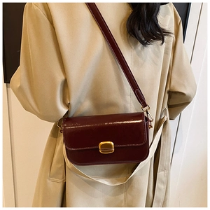 Vue détaillée du sac bandoulière bordeaux avec boucle dorée sur un trench beige