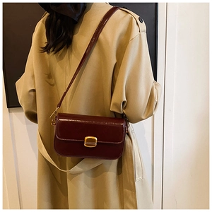 Détail du sac à bandoulière en cuir bordeaux avec boucle dorée sur trench-coat beige