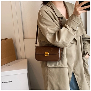 Détail d'un petit sac bandoulière marron rétro porté avec un trench-coat kaki classique