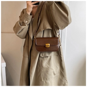 Détail d'un sac bandoulière vintage marron avec boucle dorée porté sur un trench-coat beige