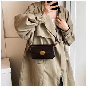 Détail du sac en cuir brillant foncé avec fermoir rotatif doré sur un trench-coat beige classique