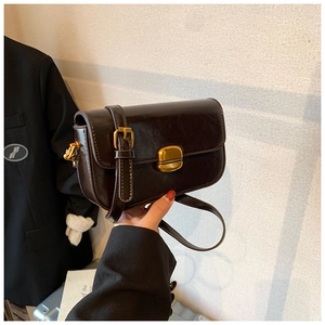 Détail d'un petit sac carré marron foncé brillant avec fermoir doré et bandoulière chaîne