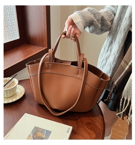 Close-up of brown litchi grain leather tote bag with thick stitching on wooden background