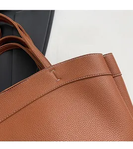 Close-up of brown leather tote bag showing white manual stitching and lychee grain texture