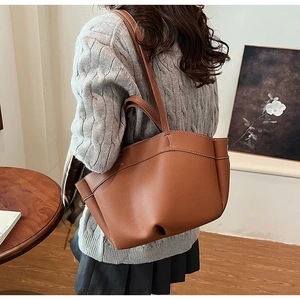 Detailed view of brown leather tote bag with white stitching and pebbled texture