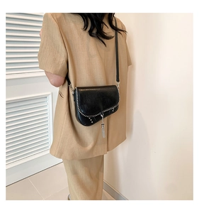 Détail du sac selle noir avec clous argentés et franges sur un blazer beige