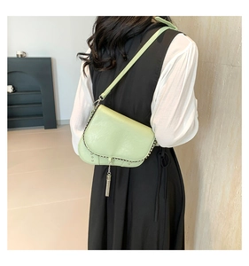 Détail d'un sac selle vert clair avec des clous métalliques et un gland à franges sur un modèle