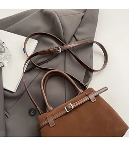 Detail view of brown matte leather shoulder bag with adjustable strap and buckle on grey suit