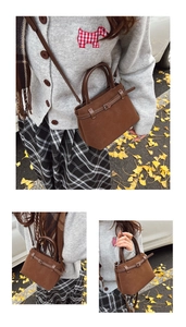 Close-up of brown suede tote bag featuring decorative belt buckle and cylindrical handles