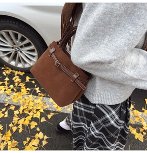 Close-up of brown suede square bag with metal buckle on autumn ginkgo leaf background
