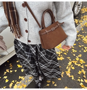 Close-up of a vintage dark brown suede handbag styled with autumn gingko leaves and a skirt
