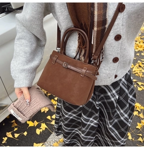 Detail of dark brown matte leather tote bag featuring metal buckle and crossbody strap