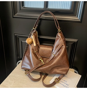 Close-up of brown faux leather tote bag with gold buckles and mini helmet charm
