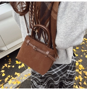 Detailed view of a brown suede handbag with top handle and decorative leather strap detail