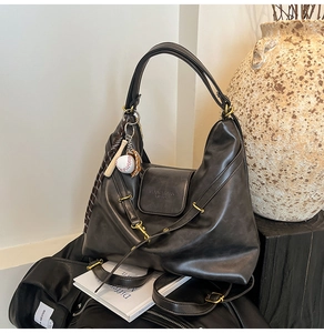 Detail of black tote bag featuring matte leather texture, gold hardware, and baseball charm