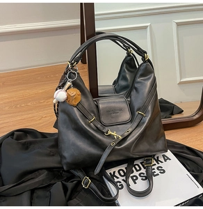 Detail of a large black leather tote bag with Muon Shark logo and baseball glove charm