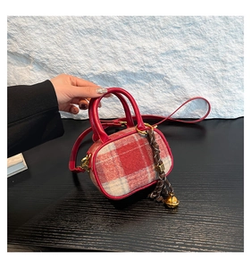 Detail of red plaid wool handbag with golden bell charm and leather shoulder strap