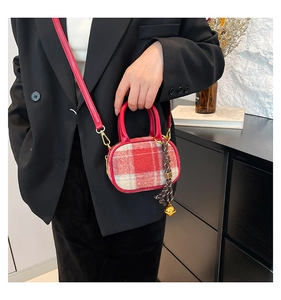 Detail of red plaid mini bowling bag featuring gold buckles and woven bell charm