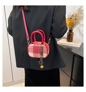 Detail of red plaid mini bowling bag with leather handle and bell charm on a model