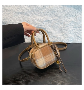 Macro detail of plaid fabric texture and leather handle with metal bell charm on handbag