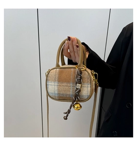 Detail of checkered wool handbag featuring brown leather trim and metallic bell charm