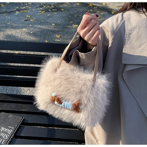 Détail du sac bandoulière en peluche beige avec broderie chien sur un banc