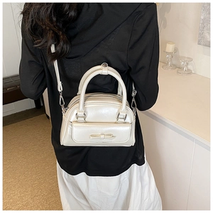 Detail view of cream pearl bow shoulder bag shown with model in home setting