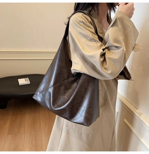 Model wearing a large dark brown leather tote bag with unique geometric stitching
