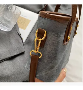 Close-up of retro gray denim bucket bag with brown leather trim and gold hardware detailing
