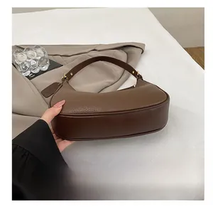 Detailed view of dark brown leather underarm bag with gold logo and textured stitching