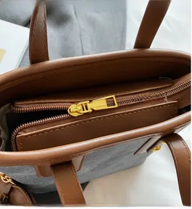 Detail of smooth gold zipper and leather trim on a grey textured bucket bag