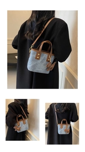 Detail of denim blue bucket bag with brown leather straps and gold rivets on a model