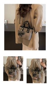 Detail of grey textured bucket bag with dog charm and gold rivets on brown suit model