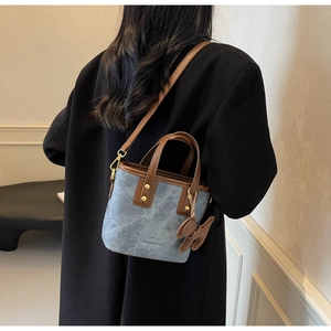 Detail of blue denim bucket bag with brown leather trim and fashion pendant accessory