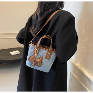 Detail of blue denim bucket bag with brown leather handles and cute dog charm ornament