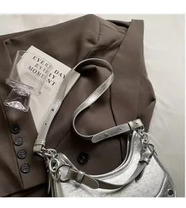 Detail view of silver cracked leather saddle bag with chain on a brown blazer