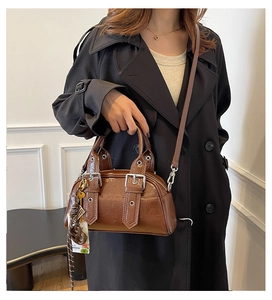 Détail d'un sac à main marron brillant avec boucle argentée et accessoire tressé