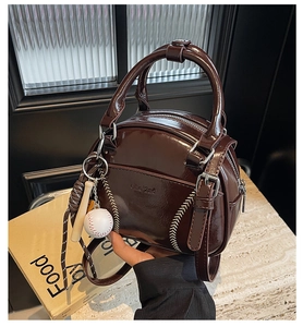 Detail of dark brown patent leather bowling bag with baseball stitching and mini charms