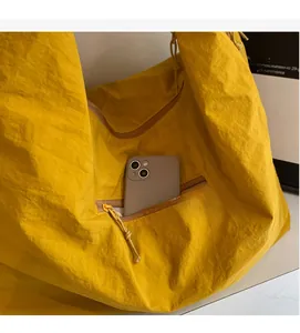 Close-up of a bright yellow nylon tote bag showing a zippered side pocket with a phone inside