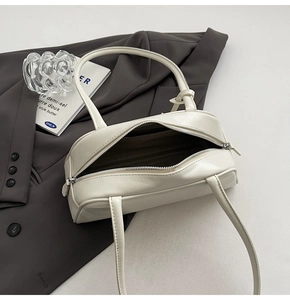 Detail of a creamy white leather Boston bag with silver zipper on a gray blazer background