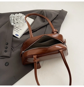 Detail of a brown glossy leather handbag with zip closure and knotted handle design