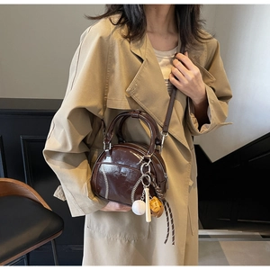 Detail of vintage brown bowling bag with baseball stitching and charm on trench coat