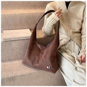 Detail of a large brown suede hobo tote bag featuring a silver irregular metal emblem