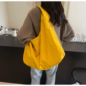 Detail of a bright yellow lightweight puffy hobo bag worn by a model in a modern cafe