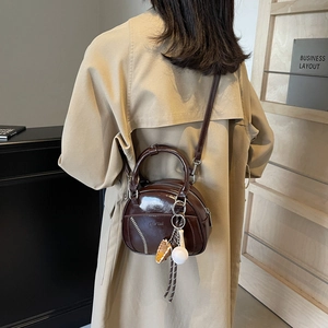 Deep brown glossy bowling bag with baseball charms worn as a crossbody shoulder bag