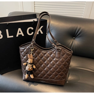 Detail of dark brown quilted tote bag with smooth finish and a knitted rabbit pendant