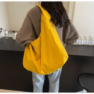 Close-up of bright yellow lightweight puffer bag with wide shoulder strap on person