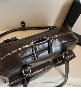 Detail of dark brown polished leather bowling bag showing silver zippers and metal hardware